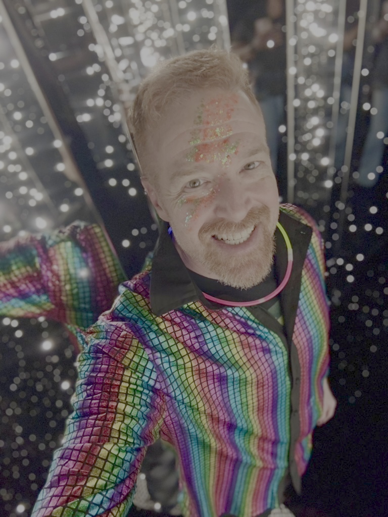 Andrew in a rainbow sequin jacket with glitter face art on Electric Night